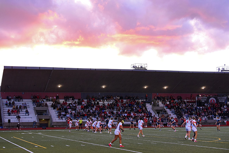 The women's rugby team competing in an evening game at sunset, with a view showing the stadium seating structure.